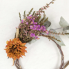Corona de flor seca. La base és feta d'eucaliptus. Incorpora caluna, limonium i una dàlia taronja